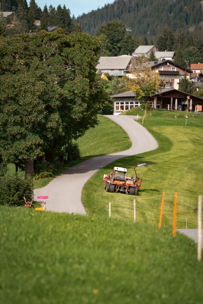 A winding road in a rural setting with a tractor, trees, and houses.